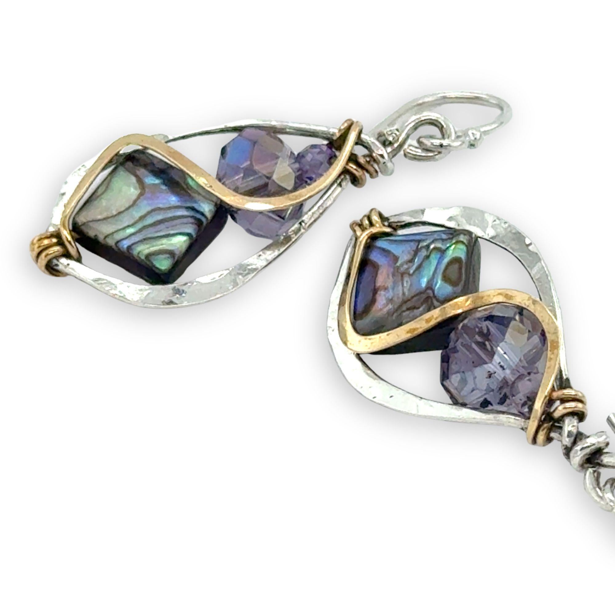 Pair of earrings with purple crystals and abalone gemstones and silver and gold accents on a white background