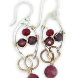 Pair of earrings with garnet gemstones and gold and silver wirework on a white background