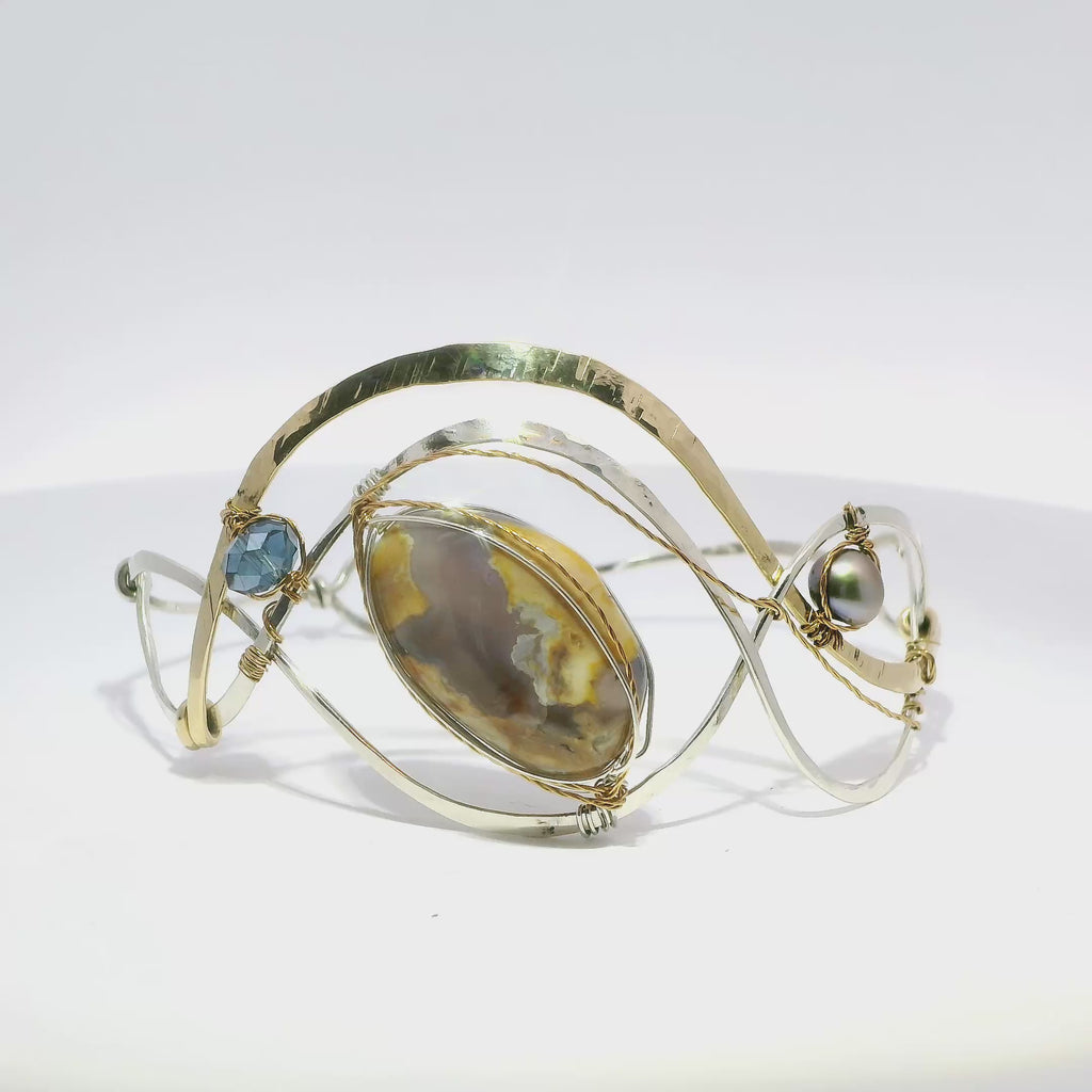 light purple chalcedony smooth nugget surrounded by layers of hammered sterling silver and brass wires to form a statement bracelet accented with fresh water pearl and crystal