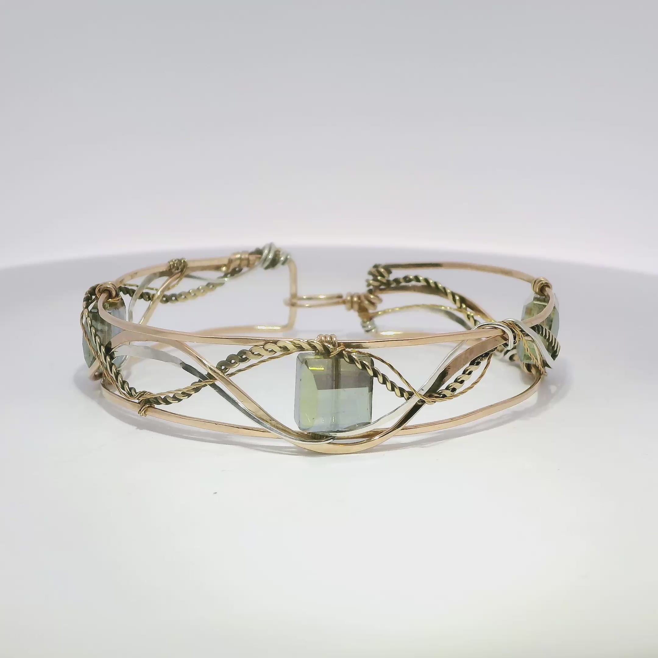 neutral green colored faceted crystals held in braided layers of sterling silver, bronze and twisted brass hammered wires all inside a bronze cuff handmade bracelet