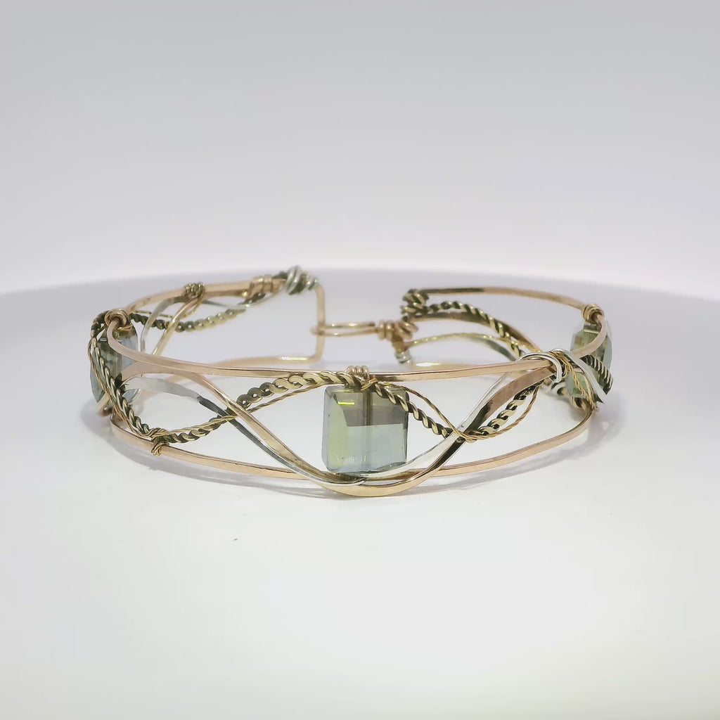 neutral green colored faceted crystals held in braided layers of sterling silver, bronze and twisted brass hammered wires all inside a bronze cuff handmade bracelet