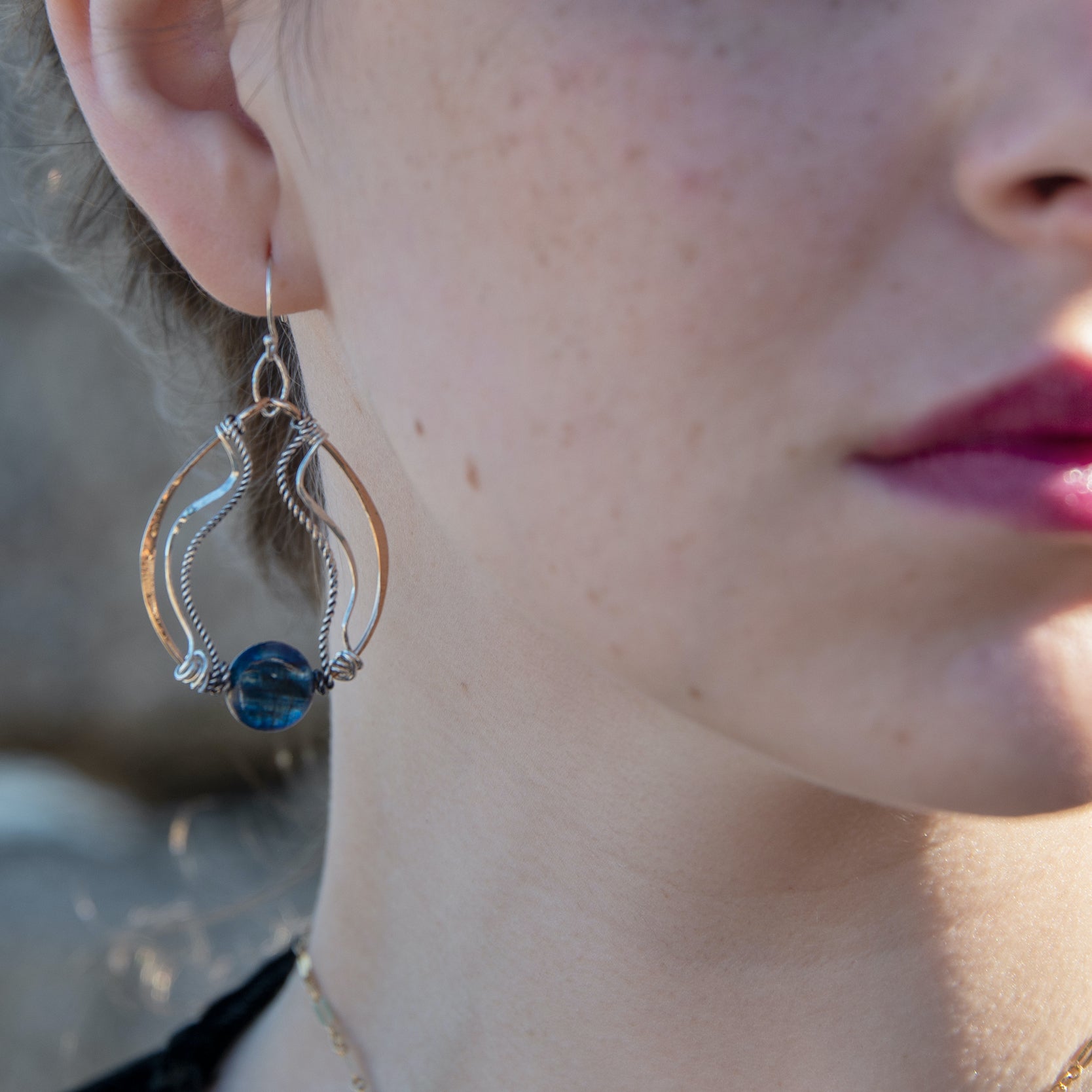 A bronze hoop earring with sparkly sterling silver and oxidized twisted sterling silver swishes holding a blue kyanite stone.