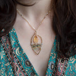 Smooth citrine drop hangs above layers of green crystal and orange crystal and luminescent citrine gemstones inside a hammered handmade brass drop necklace on sterling silver and gold filled doubled up chain