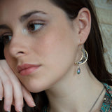 Handmade brass moon earrings with labradorite, iolite, pyrite, and crystal gemstones inside with a blue faceted crystal drop hanging from the bottom