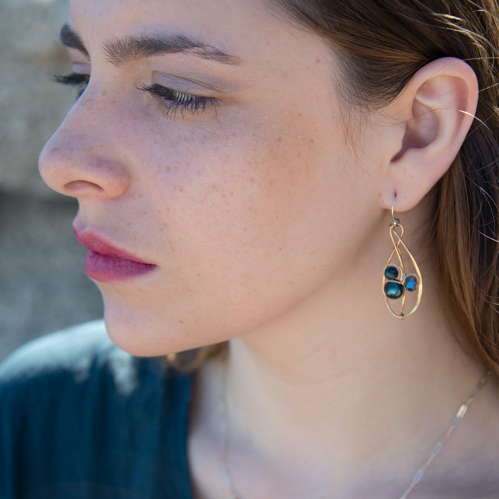 Green pearl, faceted bloodstone gemstone, and blue green crystal are nestled within brass infinity earrings on gold filled wire