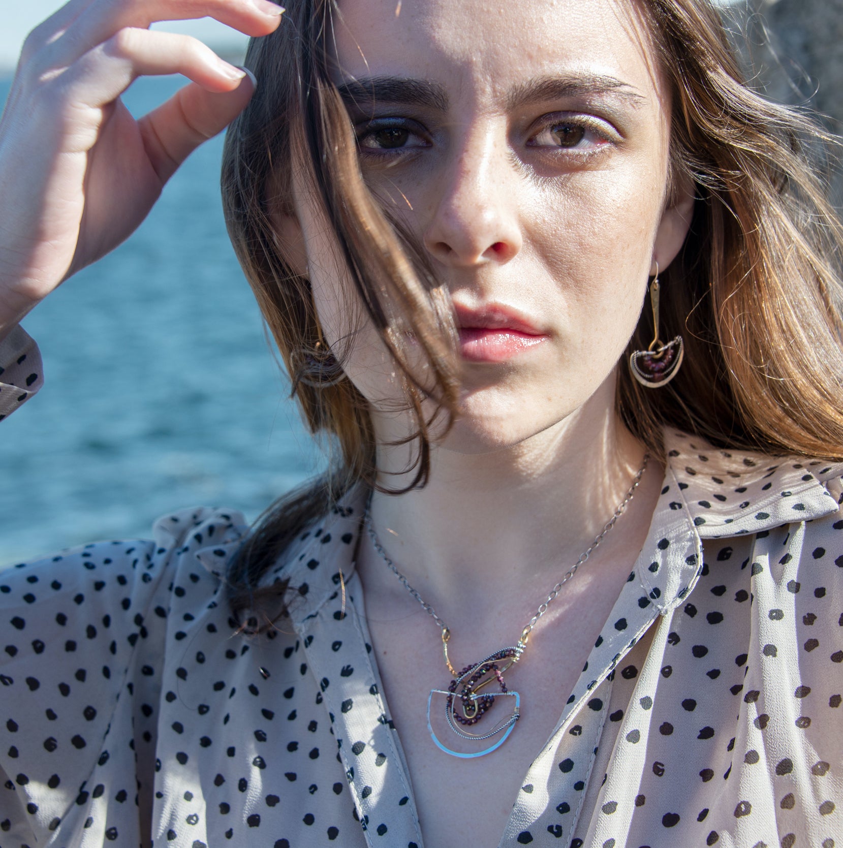 Faceted garnet gemstones braided within a sterling silver and brass fan necklace with oxidized sterling twisted wire on a delicate darkened chain