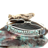 A sterling silver cuff bracelet featuring labradorite luster faceted gemstone cubes, and lines of mint crystal and pyrite, displayed on a sterling silver cuff bracelet
