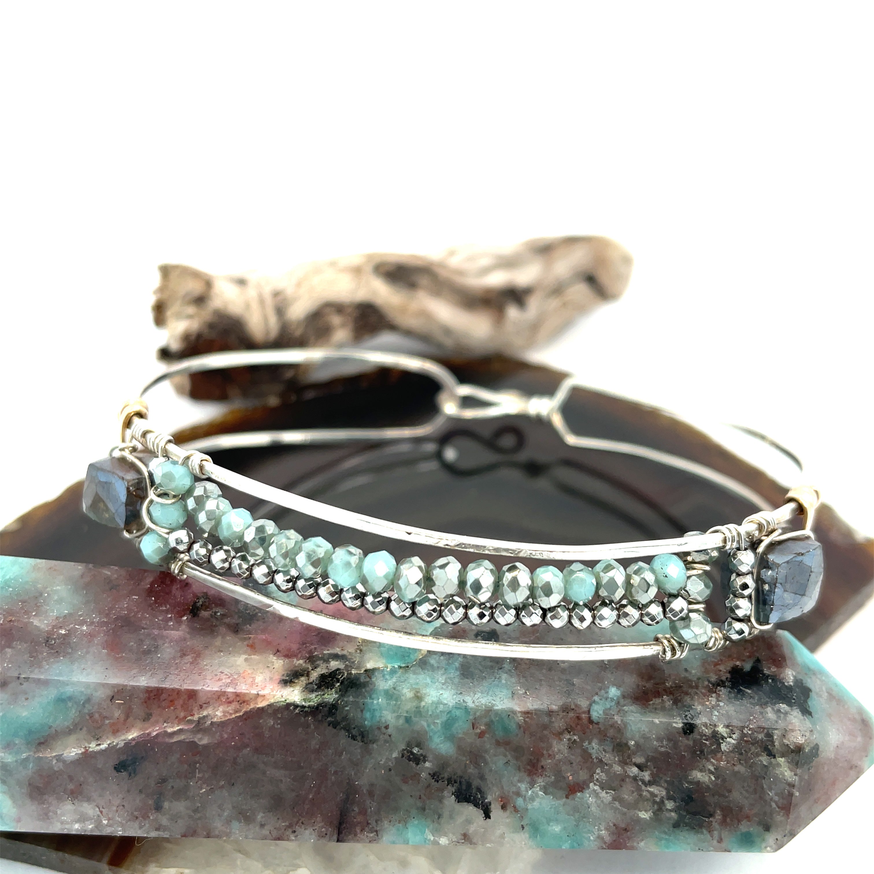 A sterling silver cuff bracelet featuring labradorite luster faceted gemstone cubes, and lines of mint crystal and pyrite, displayed on a sterling silver cuff bracelet