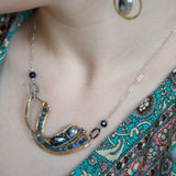 Brass statement necklace with pyrite and moonstone drops, accompanied by sodalite and pyrite gemstones laced on with sterling silver wire, accented with dark braided links within a sterling silver chain