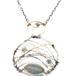 A basket weaved darkened sterling silver and brass pendant necklace featuring a flashy labradorite marquise and blue crystal accents on gold filled wire 