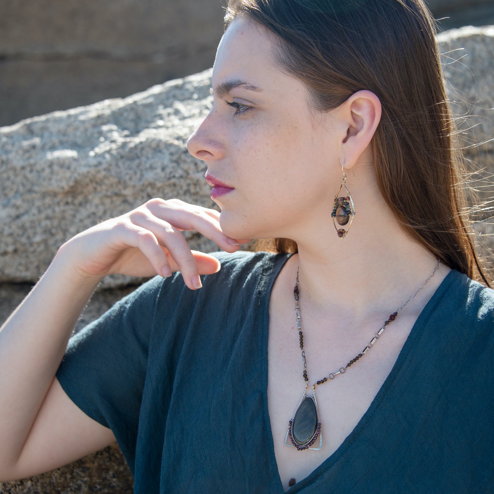 a long brass triangle pendant with a tear drop chrysoberyl cat's eye drop and oxidized sterling silver twist and garnet surrounding it. chunky and delicate chain