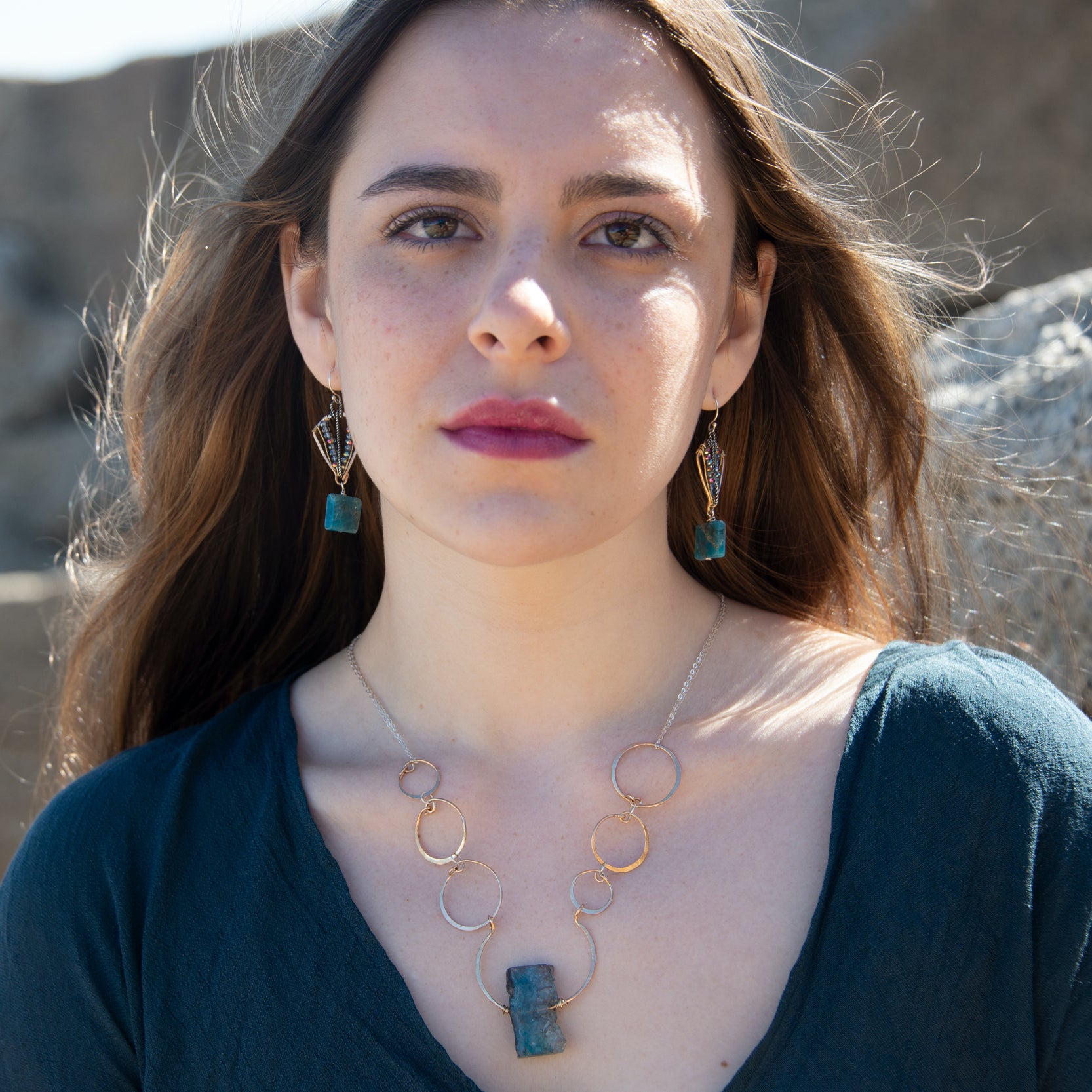 A bronze statement necklace made up of various sized rings with a blue quartz raw slab gemstone  on sterling silver delicate doubled chain