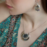 Faceted labradorite oval gemstones within a sterling silver pendant filled with pyrite gemstones and blue purple crystals and brass twist wire