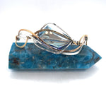 A large blue crystal is nestled within layers of braided hammered sterling silver, brass, and bronze wires to form a handmade statement cuff bracelet