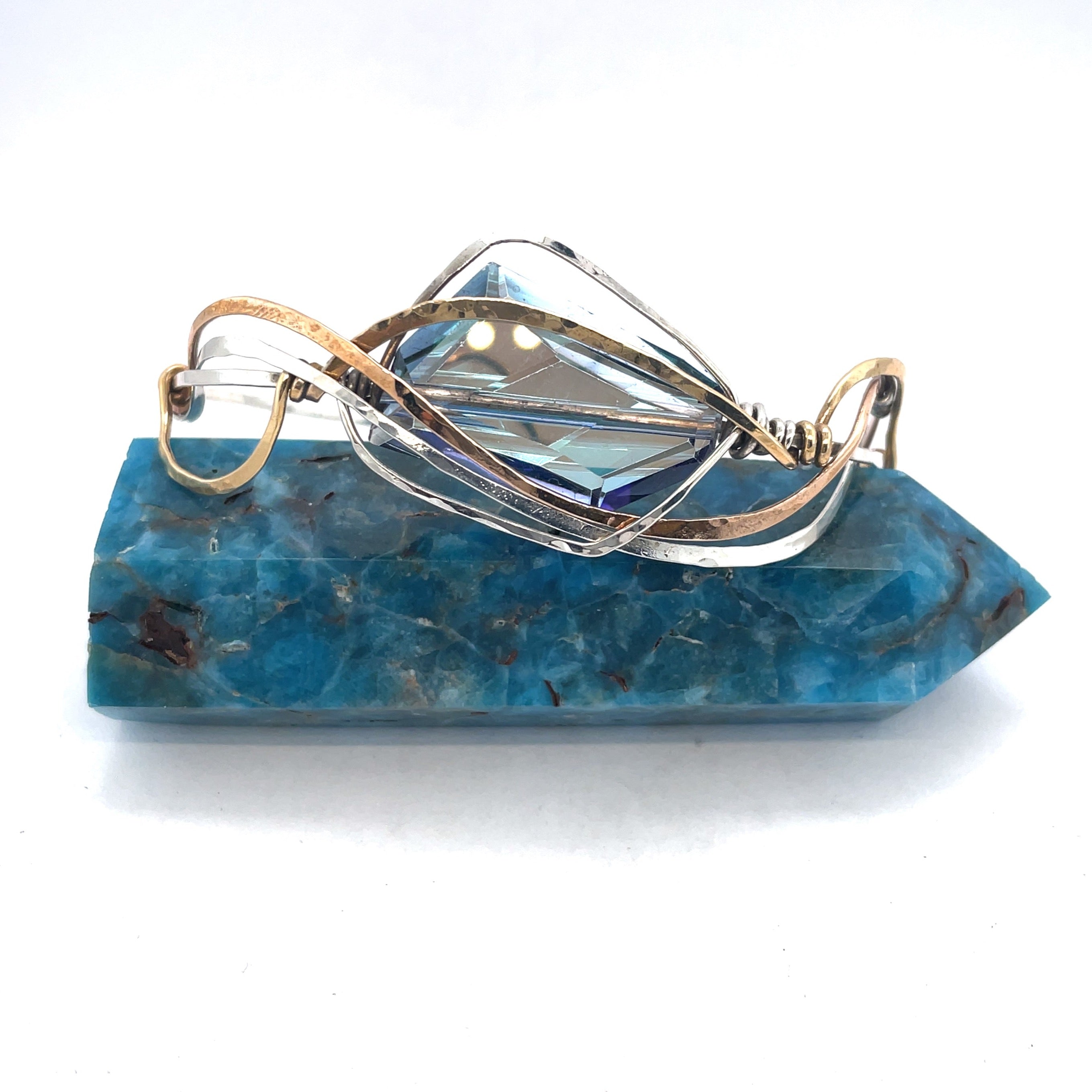 A large blue crystal is nestled within layers of braided hammered sterling silver, brass, and bronze wires to form a handmade statement cuff bracelet