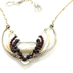 A moonstone and faceted garnet gemstones encrust wings of brass and sterling silver necklace with a gold filled chain and a signature clasp.