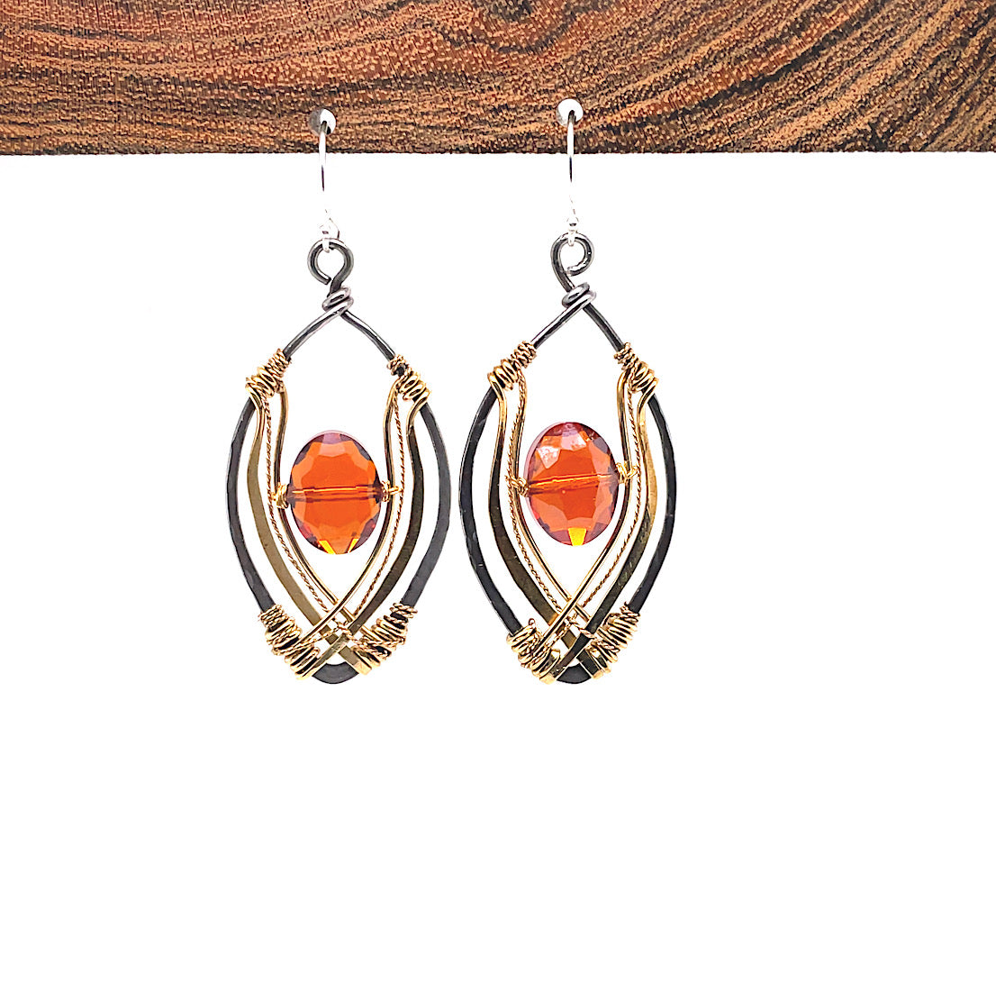 red/orange oval crystal sits inside layers of hammered brass and brass twist wire inside a darkened sterling silver marquise earring